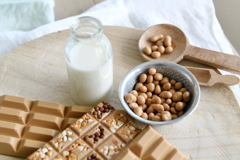 Top-down picture of a tabletop with gold chocolate tablets with inclusions, panned items, and a glass carafe of milk