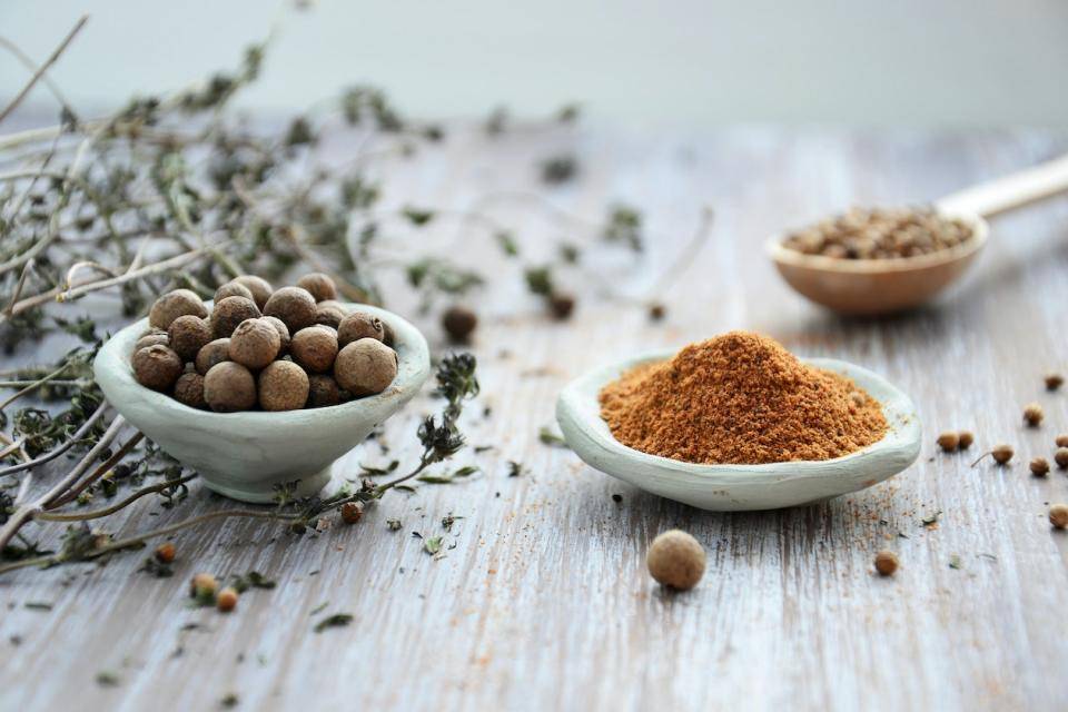 Three ceramic spoons holding different spices, leafy herb in background