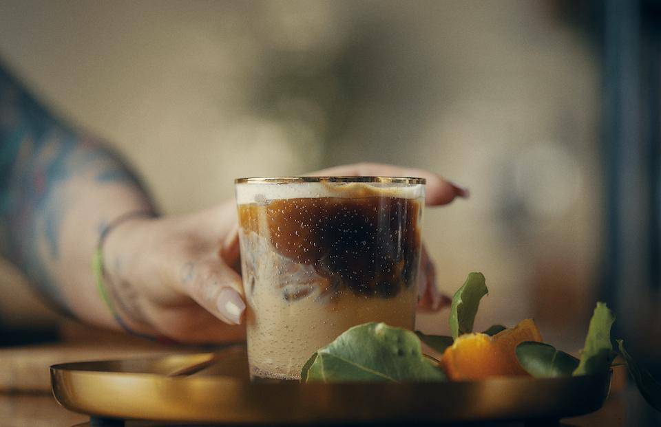 A bartender's hand places a layered chocolate drink on a tray