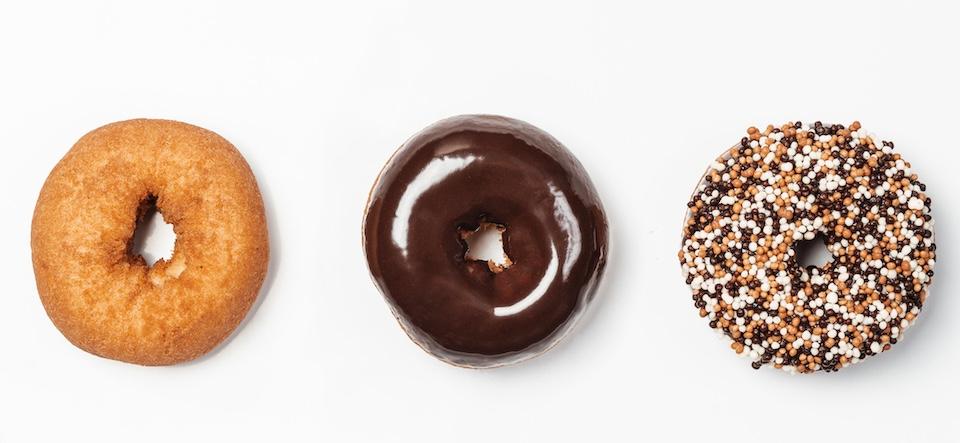 A plain doughnut, one coated in chocolate glaze, the third with crispearls covering the surface